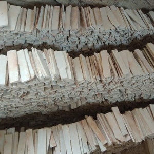 May include: Piles of rectangular, off-white stone tiles, likely for building or decorative purposes. The tiles are arranged in tidy rows, indicating a large stock. The colour is a blend of white and beige, with some tiles showing slight variations in tone.