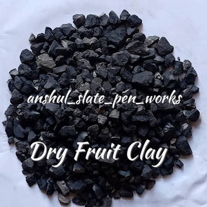 May include: A close-up of a pile of dark gray dry fruit clay. The clay is in small, irregular pieces. The text "Dry Fruit Clay" is written in white letters on the clay.