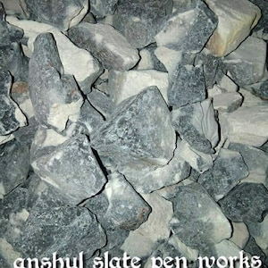 Pode incluir: Um monte de pedras de ardósia de forma irregular em tons de cinza e branco. As pedras variam em tamanho e textura, criando uma aparência natural e rústica. O texto "anshul_slate_pen_works" é visível na parte inferior da imagem.