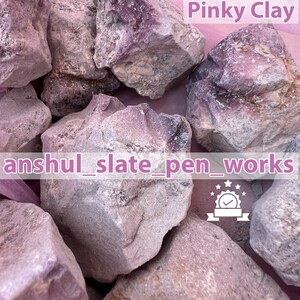 Może przedstawiać: Zbliżenie na kilka różowo-szarych skał glinianych. Obraz zawiera tekst "Pinky Clay" i "anshul_slate_pen_works". Skały mają szorstką teksturę i różne rozmiary, co wskazuje na naturalny, nieprzetworzony materiał.