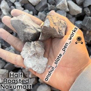 May include: Close-up of a hand holding several pieces of gray and white half-roasted nakumatt slate. The text "anshul_slate_pen_works" is written diagonally across the image.