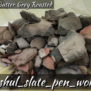 May include: A close-up of a pile of red, grey, and black slate rocks. The rocks are in a yellow bag and the text "Red Butter Grey Roasted" is at the top of the image. The text "anshul_slate_pen_works" is at the bottom of the image.