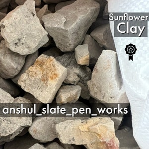 Puede incluir: Primer plano de un montón de piedras de color gris claro y marrón. Las piedras son ásperas y tienen una textura natural. El texto "Sunflower Clay" y una insignia en forma de estrella son visibles en la esquina superior derecha de la imagen. El texto "anshul_slate_pen_works" es visible en la esquina inferior izquierda de la imagen.