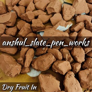 Puede incluir: Primer plano de un montón de rocas de arcilla roja. El texto "anshul_slate_pen_works" y "Dry Fruit In Red Khadi" es visible en la superficie.