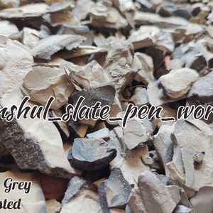 May include: A close-up of a pile of small, irregularly shaped, gray and black slate pieces. The slate is labeled "Butter Grey Roasted" and "anshul_slate_pen_works".