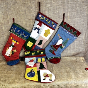 May include: Four fabric Christmas stockings featuring patchwork designs. One displays a snowman and the text Let it Snow. Another shows a snowman and gingerbread man with the text MERRY. A third features Santa with a tree. The fourth shows Santa and a reindeer with the text HO HO HO.