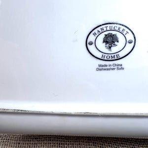 Puede incluir: Una fuente rectangular de cer&aacute;mica blanca con un logotipo ovalado negro que dice "Nantucket Home". El logotipo presenta un &aacute;rbol y las palabras "Made in China Dishwasher Safe".