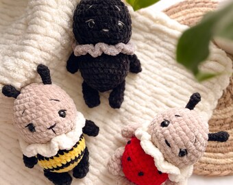 May include: Three crocheted plush toys in the shape of insects. A black bug with a gray ruffle collar, a bee with a yellow and black striped body, and a ladybug with a red body and black spots.