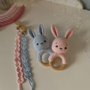 May include: Two crocheted bunny rattle toys with wooden rings. One bunny is light blue and the other is pink. Both bunnies have black embroidered eyes and noses.