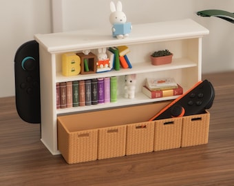 Könnte beinhalten: Ein weißes Miniatur-Bücherregal mit zwei Ebenen, gefüllt mit winzigen Büchern, einer kleinen weißen Hasenfigur und einer Topfpflanze. Die Basis enthält fünf beige Aufbewahrungsboxen in Flechtoptik, mit schwarzen Controllern an den Seiten.