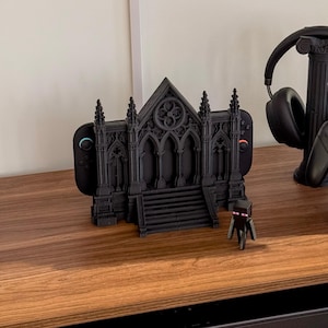 May include: A black 3D-printed gothic cathedral-style gaming console dock, a black headphone stand shaped like a classical column, a black game controller stand, a black game controller, a pair of black headphones, and a small black Enderman figure.