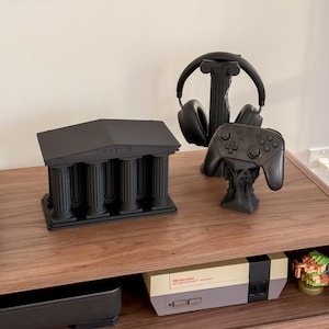 May include: Black gaming accessories, including a controller and headset, displayed on a wooden surface. A black structure resembling a Greek temple with the word "SWITCH" is also present. A Nintendo console is visible below.