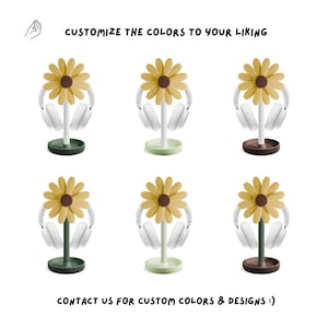 May include: Six different color variations of a sunflower-shaped headphone stand. The stand is made of plastic and has a white headphone holder. The sunflower is yellow with a brown center. The stands are available in green, brown, and light green.
