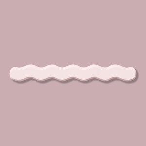 May include: A light pink, wavy-edged decorative object, possibly a shelf or wall decor, against a muted mauve background. The object has a smooth, matte finish and casts a subtle shadow, creating a sense of depth. The design is minimalist and modern.