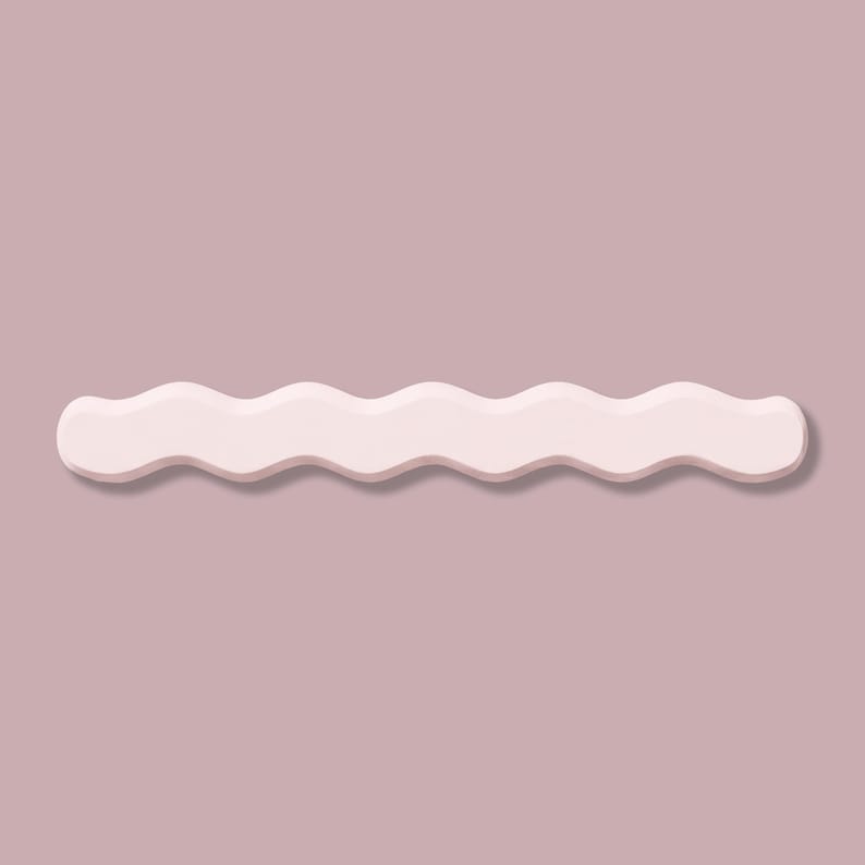 May include: A light pink, wavy-edged decorative object, possibly a shelf or wall decor, against a muted mauve background. The object has a smooth, matte finish and casts a subtle shadow, creating a sense of depth. The design is minimalist and modern.