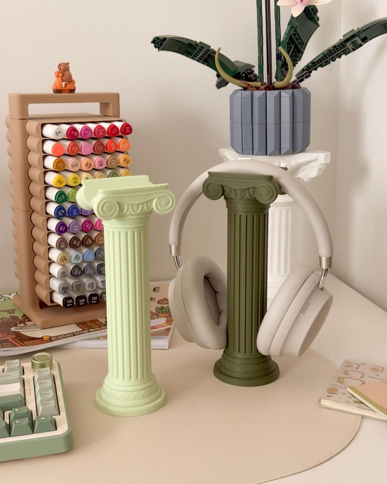 Puede incluir: Dos columnas decorativas, una verde claro y otra verde oliva. Un par de auriculares blancos descansa sobre la columna verde oliva. Tambi&eacute;n se ven un portal&aacute;pices marr&oacute;n y un teclado.