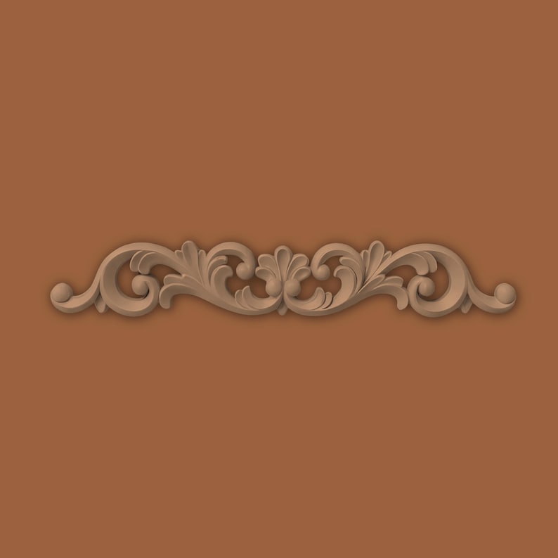 May include: A decorative wood carving with a symmetrical, scrolling floral design. The carving features stylized leaves and curls, with a light brown colour, set against a solid brown background. The design is centered horizontally.
