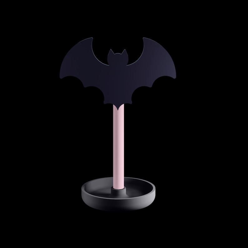 K&ouml;nnte beinhalten: Schwarze fledermausf&ouml;rmige Dekoration mit rosa Stiel und rundem, dunkelgrauem Sockel. Die Fledermaus hat detaillierte Fl&uuml;gelausschnitte. Schlichtes, modernes Design, perfekt f&uuml;r Halloween oder Gothic-Dekoration.