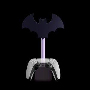 K&ouml;nnte beinhalten: Ein schwarz-wei&szlig;er Gaming-Controller ruht auf einem lila St&auml;nder mit einer Fledermaus-Silhouette. Der St&auml;nder ist so konzipiert, dass er den Controller h&auml;lt, mit einem dunkelvioletten Sockel und einem hellvioletten Stiel.