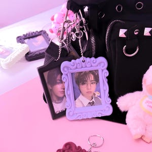 May include: A black bag with silver hardware and a variety of decorative keychains. The keychains include small picture frames in various colors, each holding a photograph. A small stuffed animal is also attached to the bag.