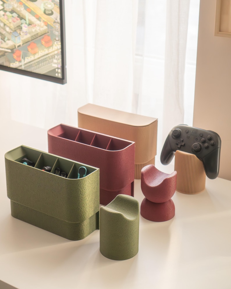 May include: A collection of modern desk organizers in various colors. The set includes a green organizer with compartments, a burgundy organizer, a tan organizer, and a red and green stand. A black game controller rests on a wooden stand.
