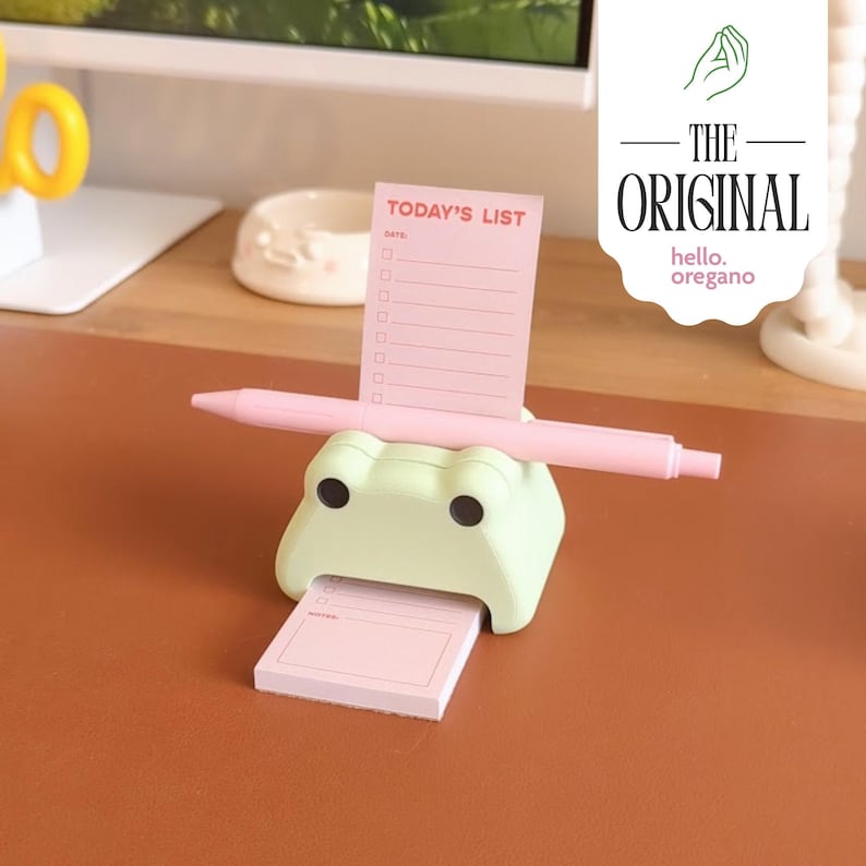 May include: A green frog-shaped desk organizer with a pink pen holder and a pink notepad with the text "TODAY'S LIST" and a checklist.
