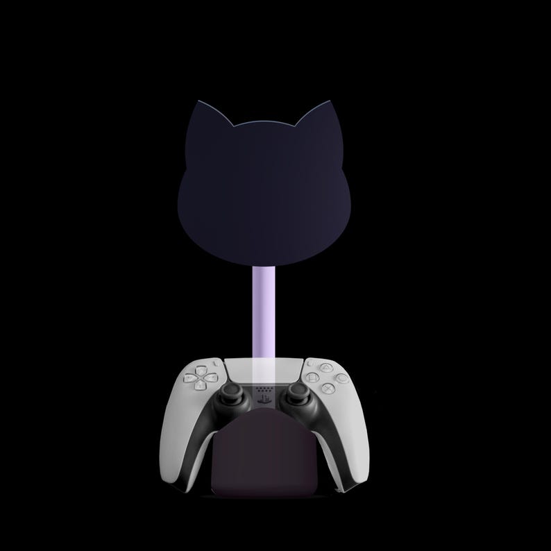 Puede incluir: Un soporte negro con forma de gato con un tallo morado claro, dise&ntilde;ado para sostener un mando de juego blanco y negro. El soporte est&aacute; dise&ntilde;ado para sujetar el mando en su sitio. El fondo es negro.