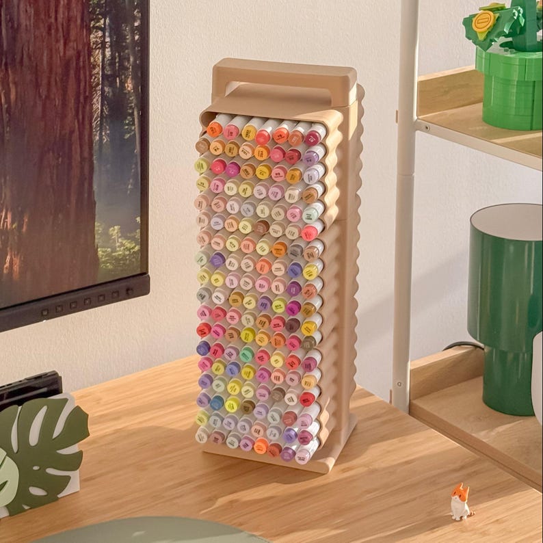May include: A beige marker organizer filled with a variety of colorful markers. The organizer has a handle and a wavy design on the sides. The markers are arranged in rows, showcasing a spectrum of colors, perfect for art supplies.