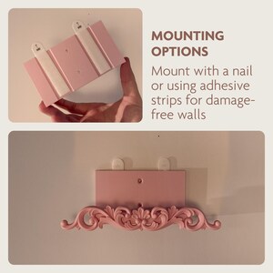 May include: Pink wall shelf with decorative scrollwork. The shelf can be mounted with a nail or adhesive strips. The image shows the shelf being held and mounted on a wall. Text on the image reads "MOUNTING OPTIONS".