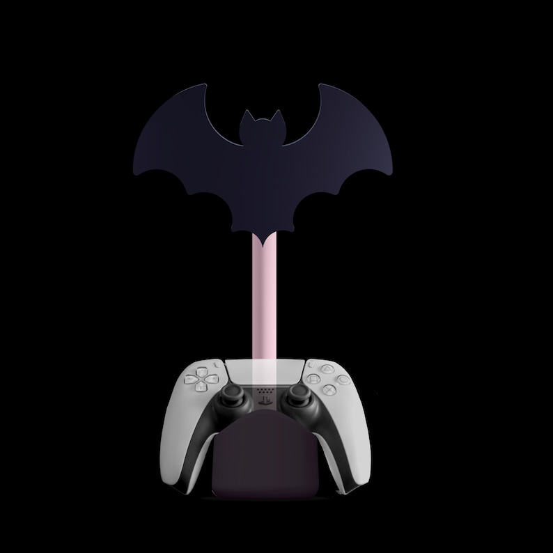 K&ouml;nnte beinhalten: Ein schwarzer, fledermausf&ouml;rmiger Controller-St&auml;nder mit rosa Stiel, der einen wei&szlig;-schwarzen Gamecontroller h&auml;lt. Der St&auml;nder ist f&uuml;r einen Gamecontroller konzipiert und hat eine Fledermaus-Silhouette.