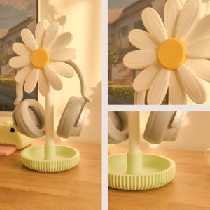 May include: A white daisy-shaped headphone stand with two gray headphones hanging from it. The stand has a green base.