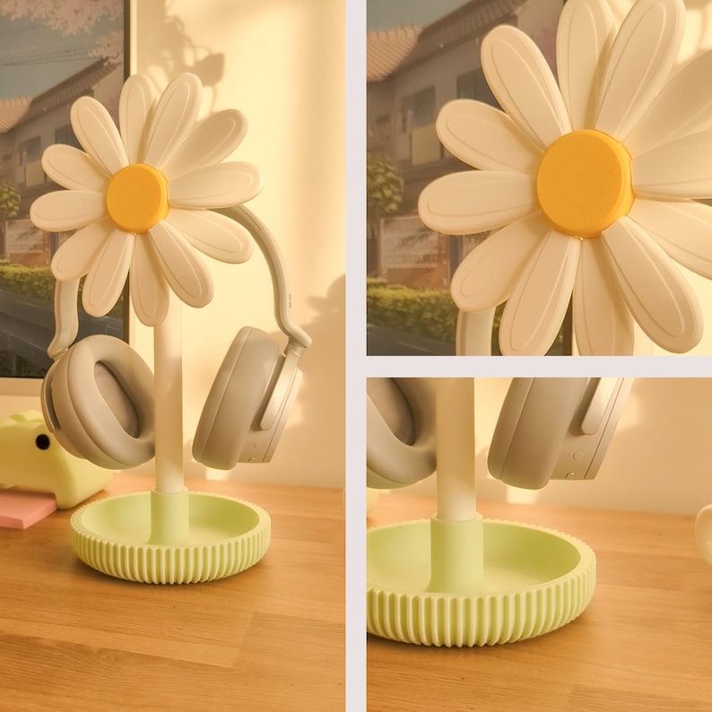 May include: A white daisy-shaped headphone stand with two gray headphones hanging from it. The stand has a green base.