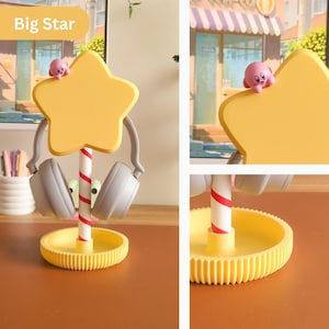 May include: A yellow star-shaped headphone stand featuring a pink character figure. The stand has a white and red striped pole and a round yellow base. The text "Big Star" is in the upper left corner. Grey headphones are hanging on the stand.