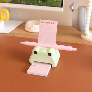 May include: A green frog-shaped desk organizer with a pink pen and a pink notepad that says "TODAY'S LIST" with a section for notes.