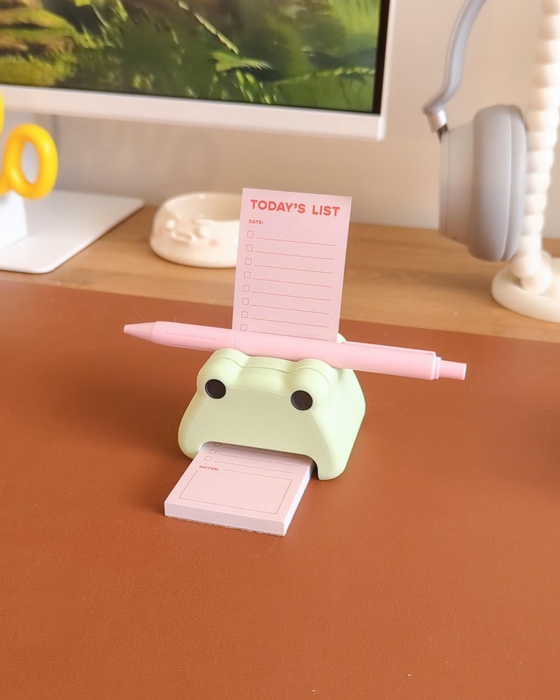 May include: A green frog-shaped desk organizer with a pink pen and a pink notepad that says "TODAY'S LIST" with a section for notes.