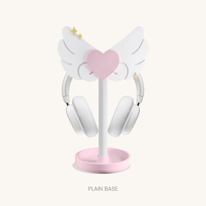 May include: White headphone stand with a pink heart and wings. The base is pink and the stand is white. The text "PLAIN BASE" is printed below the stand.