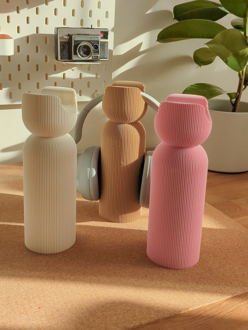 May include: Three decorative bottles with a ribbed design. The bottles are white, beige, and pink. The bottles are sitting on a cork surface.