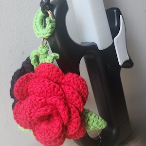 May include: A black lighter with a white body and the text "The Rose" is displayed. A handmade red crochet rose with green leaves and a black crochet backing is attached to the lighter.