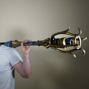 以下が含まれることがあります： 黒色のハンドルが付いた、大きく装飾的な金色の杖を持った人。杖は、頂上にリングが付いた、装飾的で複雑なデザインをしています。