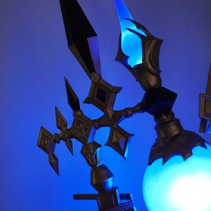 May include: A decorative lamp with a blue light orb and intricate metalwork. The lamp features a black and gold design with a pointed, angular shape.