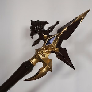 May include: A decorative spear with a gold and brown finish. The spear head features a detailed design with a blue gem in the center.