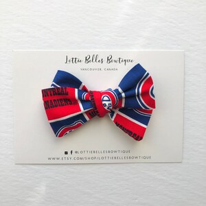 May include: A red and blue bow tie with the Montreal Canadiens logo. The bow tie is on a white card with the text "Lottie Belles Boutique, Vancouver, Canada" and social media information.