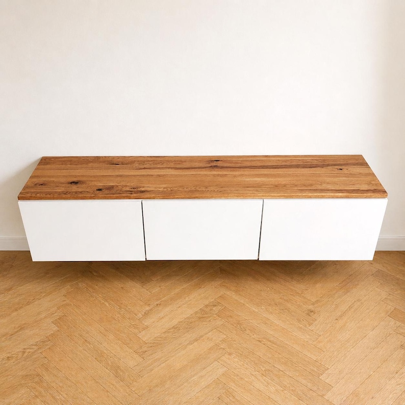 May include: A wall-mounted floating cabinet featuring a natural wood grain top surface and three smooth, solid white rectangular front panels. The unit has a horizontal rectangular shape with clean lines and a flat top, providing a storage solution.