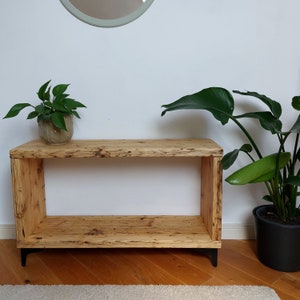 May include: A rustic wooden console table with a shelf, black metal legs, and a natural wood finish. The table is decorated with two potted plants.