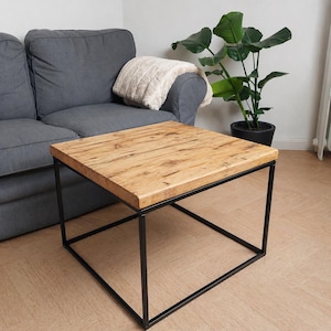 Könnte beinhalten: Quadratischer Couchtisch mit hellbrauner Holzplatte und schwarzem Metallrahmen. Der Tisch hat ein natürliches Holzmaserungsmuster und ein modernes Design. Der Tisch ist etwa 76 cm groß.