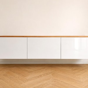 May include: A wall-mounted floating cabinet featuring three rectangular white doors with a smooth finish and a natural light brown wooden top surface. The unit is horizontally oriented and provides a clean, flat-front storage solution.