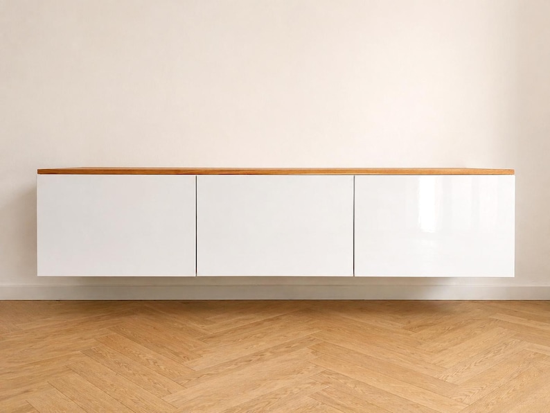 May include: A wall-mounted floating cabinet featuring three rectangular white doors with a smooth finish and a natural light brown wooden top surface. The unit is horizontally oriented and provides a clean, flat-front storage solution.