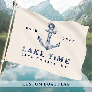 Puede incluir: Una bandera de barco color crema con un diseño de ancla azul marino y las palabras "LAKE TIME LAKE GEORGE, NY" y "ESTD 2026." La bandera está en un mástil dorado contra un fondo de montañas y agua. El texto "CUSTOM BOAT FLAG" está en la parte inferior.