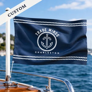 Op de afbeelding: Een rechthoekige marineblauwe vlag met een wit touwpatroon aan de boven- en onderkant. Het midden toont een wit cirkelvormig touwembleem met een ankerpictogram en de tekst TRADE WINDS en CHARLESTON. Een witte banner bevat het woord CUSTOM.