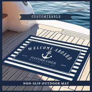 Puede incluir: Una alfombra de exterior antideslizante azul marino y blanca con las palabras "WELCOME ABOARD" y un gráfico de ancla. La alfombra también incluye el texto "DAYDREAMER WATCH HILL, RI 2024". La alfombra está sobre una cubierta de madera.